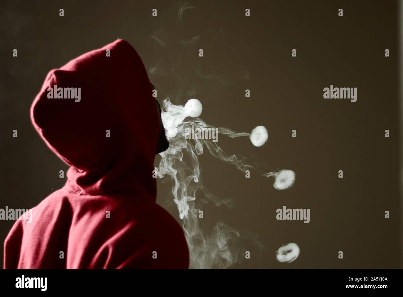 Young male in red hoodie vaping smoking, blows 4 smoke rings, isolated rear view Stock Photo
