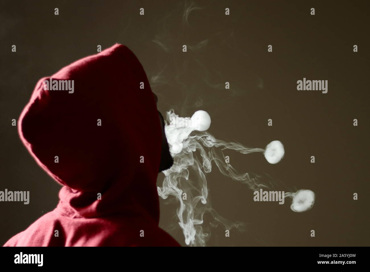 Young male in red hoodie vaping smoking, blows 3 smoke rings, isolated rear view Stock Photo