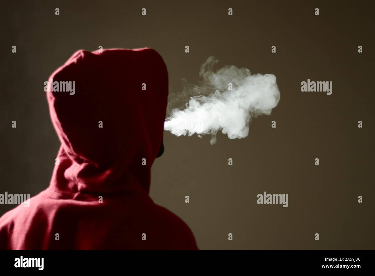 Young male in red hoodie vaping smoking, exhales thick vapor, isolated rear view Stock Photo