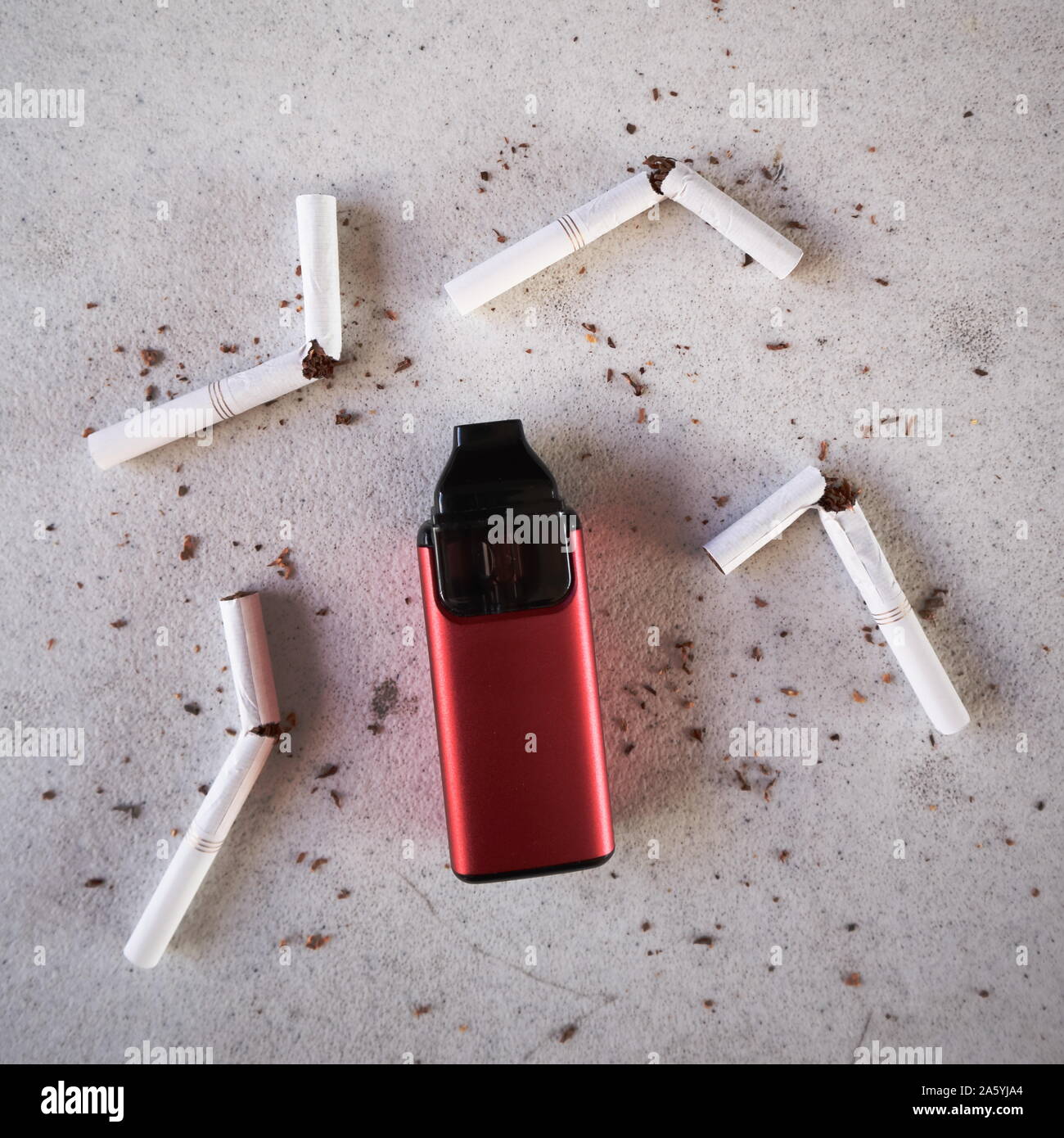 Single red vape electronic cigarette as smoking alternative with broken cigarettes and scattered tobacco on white textured background isolated Stock Photo