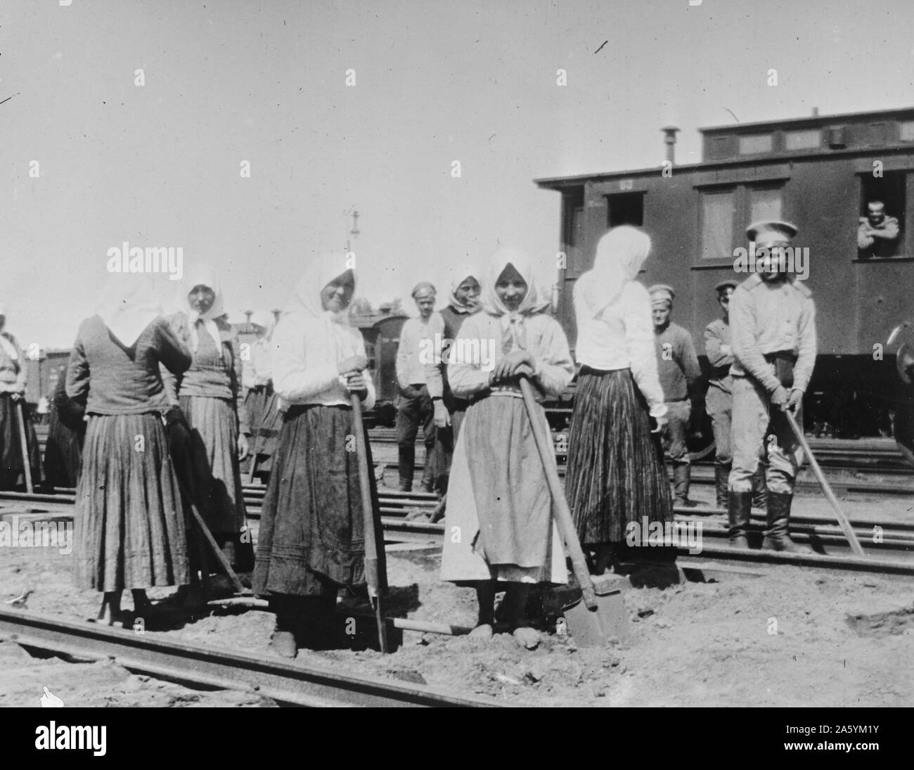 Russian women work on railway tracks as troop train stands nearby; World war One, Stock Photo