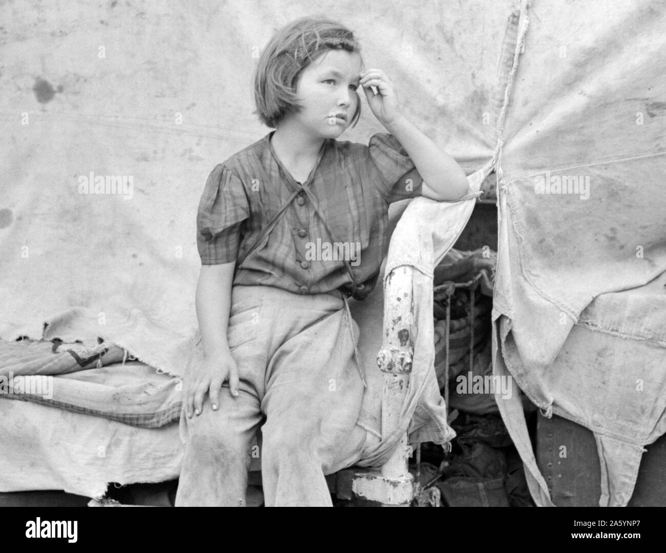 Child of migrant worker sitting on bed in tent home of cotton picking sacks, Harlingen, Texas By Russell Lee, 1903-1986, photographer 19390101 Stock Photo