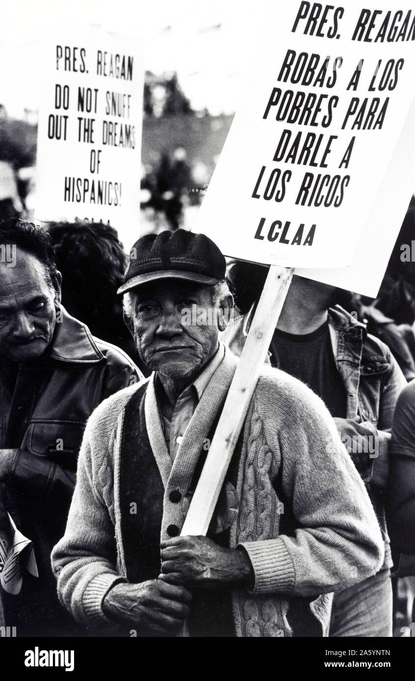 Reagan la roba a los pobres Migrant farm worker at a demonstration, Washington, D.C. Published 1981. Photograph shows an elderly man in the Solidarity Day march, holding a picket sign with the message: Pres. Reagan robas a los pobres para darle a los ricos, LCLAA, in a crowd at a protest. A sign in the background has the message: Pres. Reagan, do not snuff out the dreams of Hispanics! Stock Photo