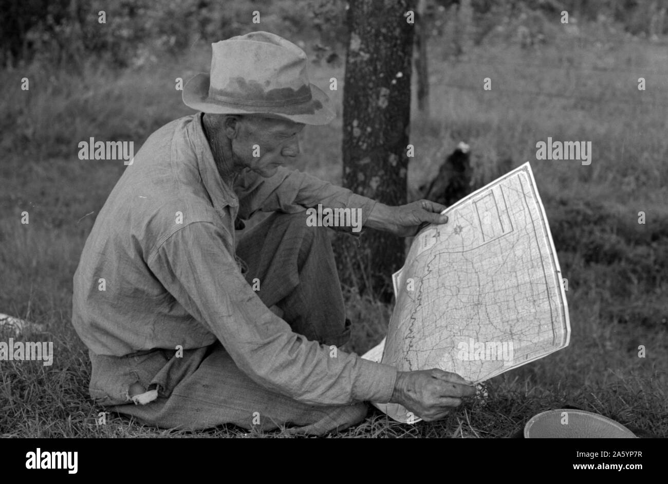 White migrant agricultural worker from Texas studying the map while stopped for lunch on the roadside east of Fort Gibson, Oklahoma By Russell Lee, 1903-1986, Published: 19390101 June. Stock Photo