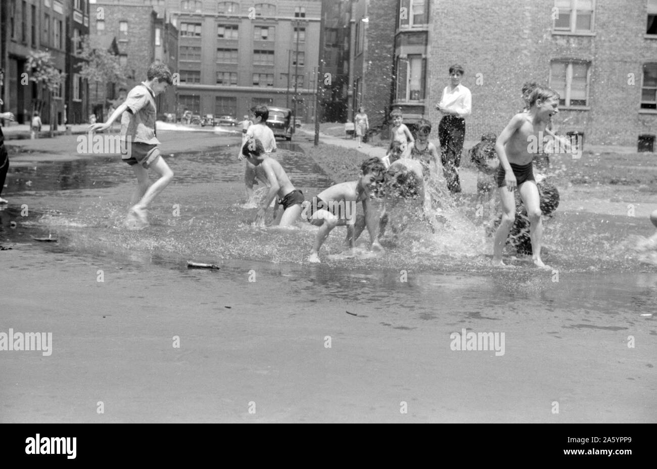 Children in a street are cooling off in water from hydrant, Chicago, Illinois. 1941. . Stock Photo