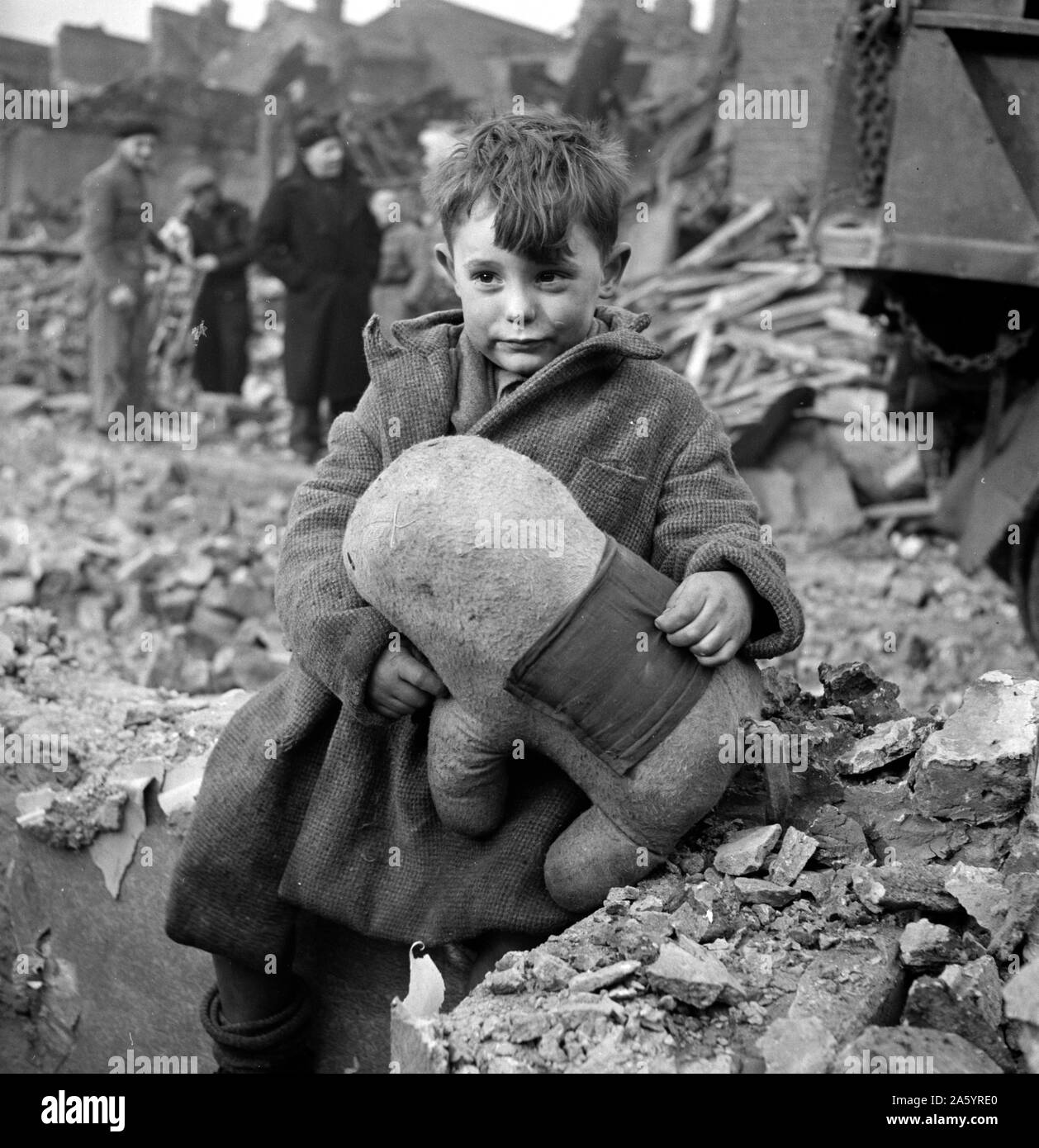 Abandoned boy holding a stuffed toy animal amid ruins following German aerial bombing of London during the Blitz of World War two Stock Photo