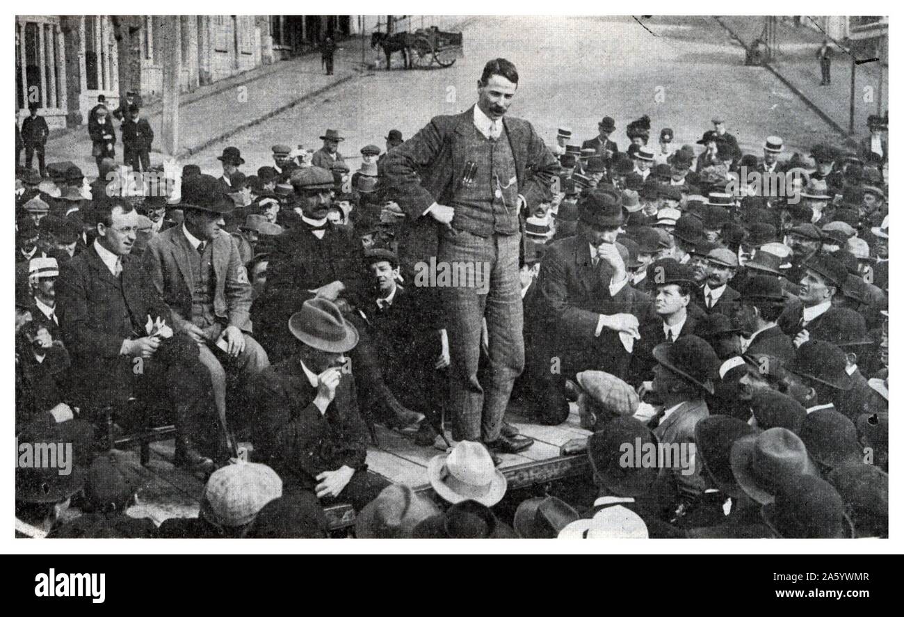 Robert 'Bob' Semple (21 October 1873 – 31 January 1955) ; union leader and later Minister of Public Works for the first Labour Government of New Zealand. Robert Semple speaking at the foot of Wakefield Street, Auckland, in October, 1911. With him are two future Prime Ministers — Peter Fraser (seated, left), and Michael Joseph Savage (kneeling, right). Semple is reported to have said: “We aim at the abolition of poverty, a more equal distribution of wealth and equal opportunities for all.” Stock Photo