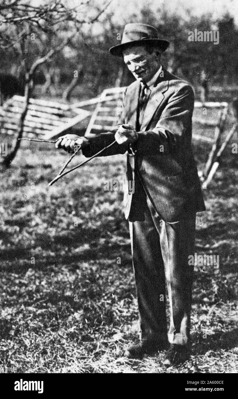 Water diviner or Dowser using a forked twig; 1930. Dowsing is a type of divination employed in attempts to locate ground water, buried metals or ores, gemstones, oil, gravesites, and many other objects and materials without the use of scientific apparatus Stock Photo