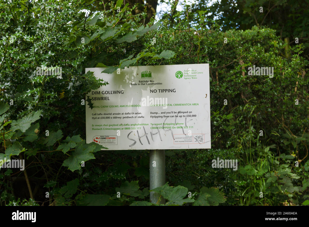 A defaced environmental crime watch area notice in English and Welsh posted by the Welsh government warning offenders of large fines for fly tipping Stock Photo