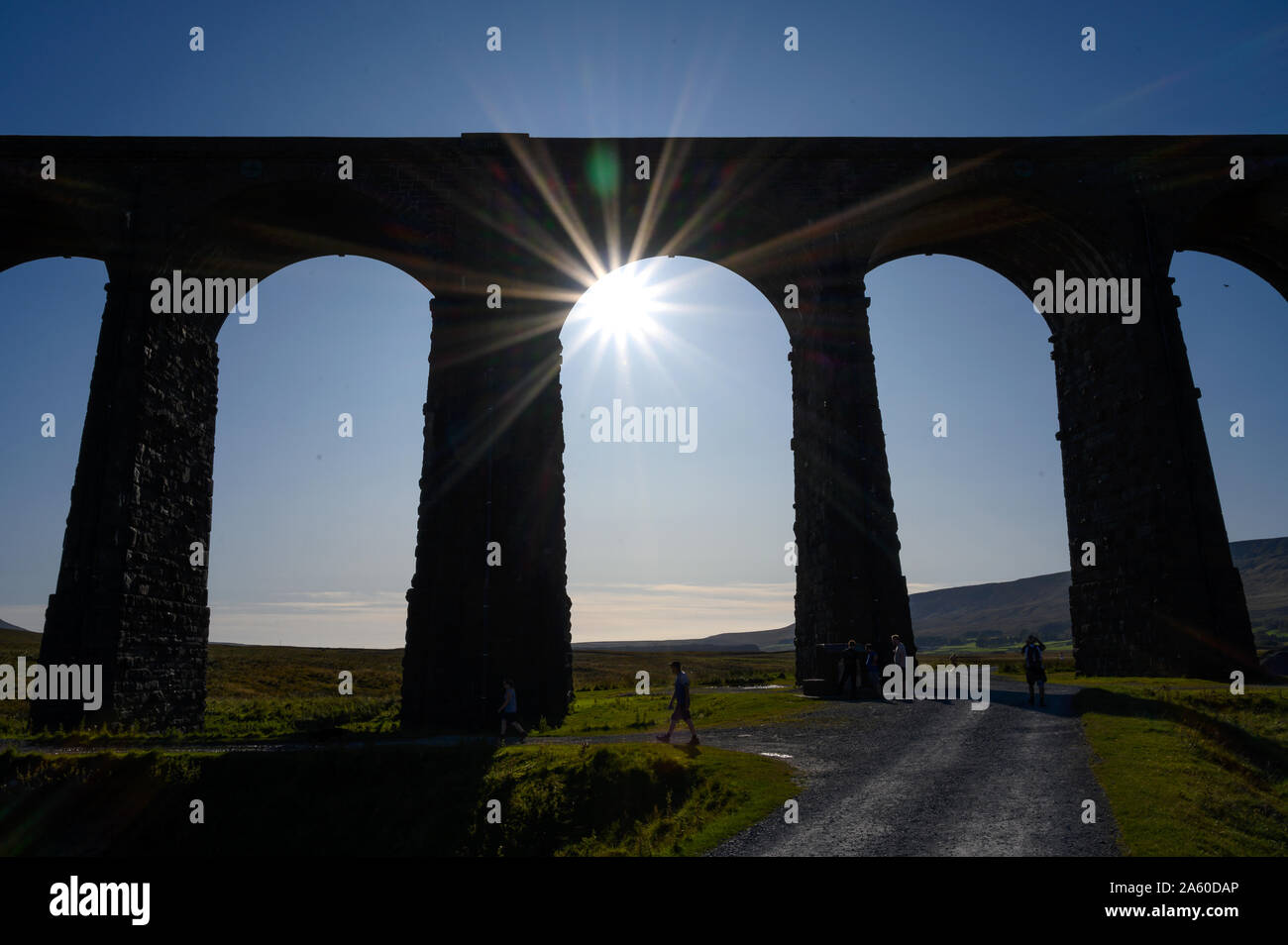 A summer sun in a blue sky visible under one of the arches of Ribblehead Viaduct on the Settle to Carlisle Railway Line, North Yorkshire. Stock Photo
