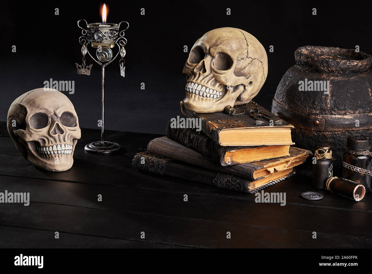 Realistic model of two human craniums with white teeth, books with spells, old pot, jars of potion, burning candle in candlestick are on a wooden dark Stock Photo