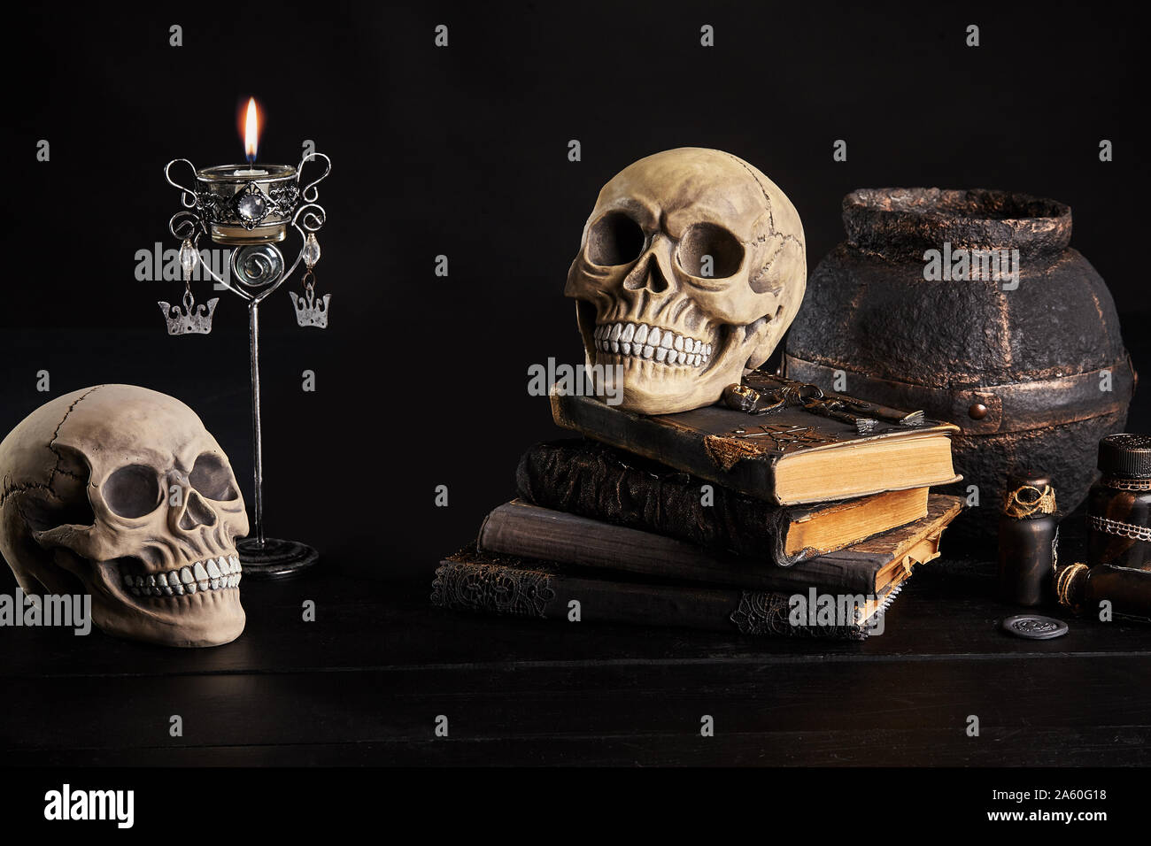 Realistic model of two human craniums with teeth, books with spells, old pot, jars of potion, burning candle in candlestick are on a wooden dark table Stock Photo