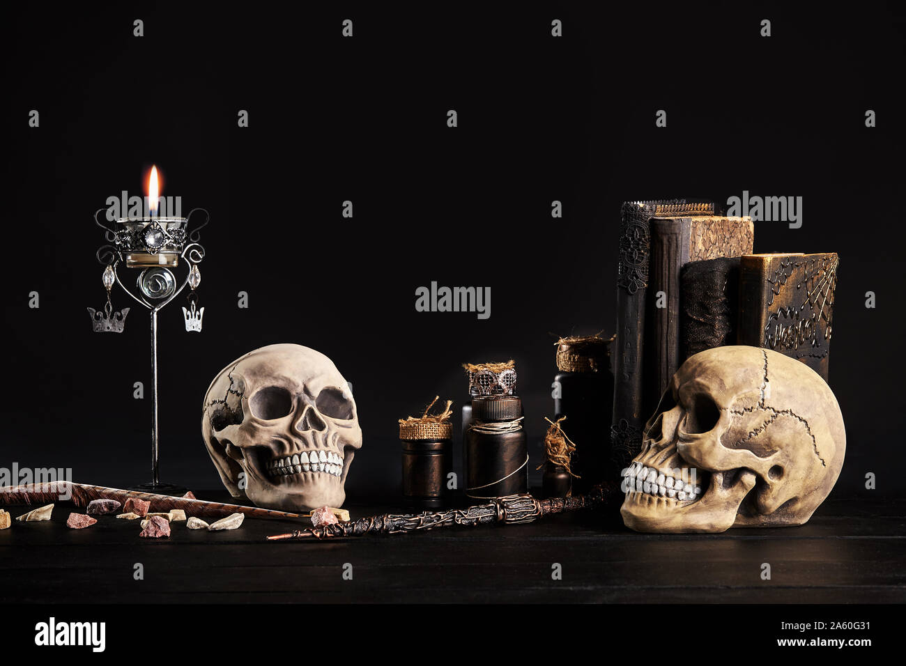 Realistic model of two human craniums with teeth, books with spells, jars of potion, burning candle in candlestick, little stones and a feather are on Stock Photo