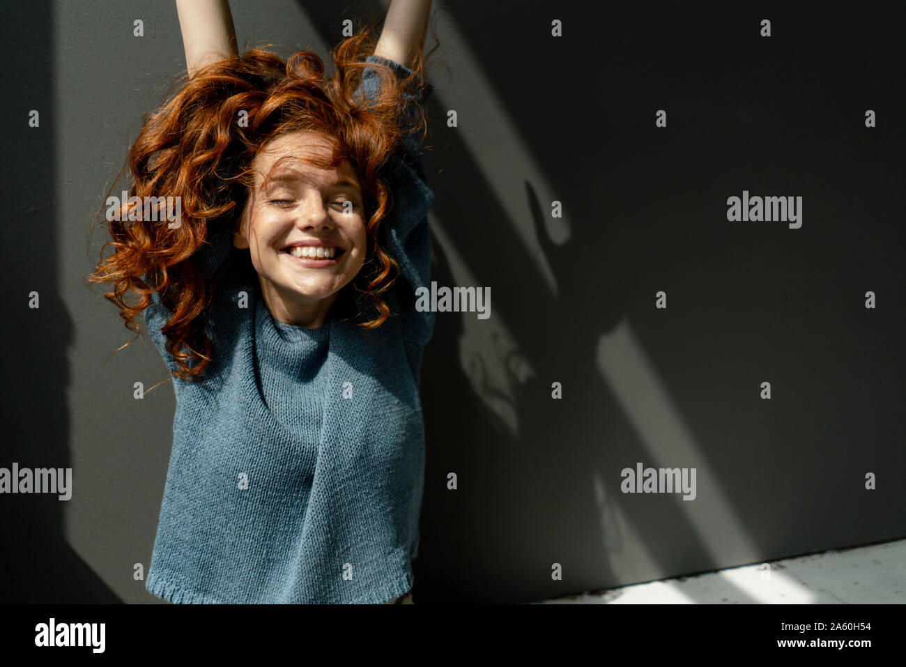 Portrait of happy redheaded woman with eyes closed raising hands Stock Photo