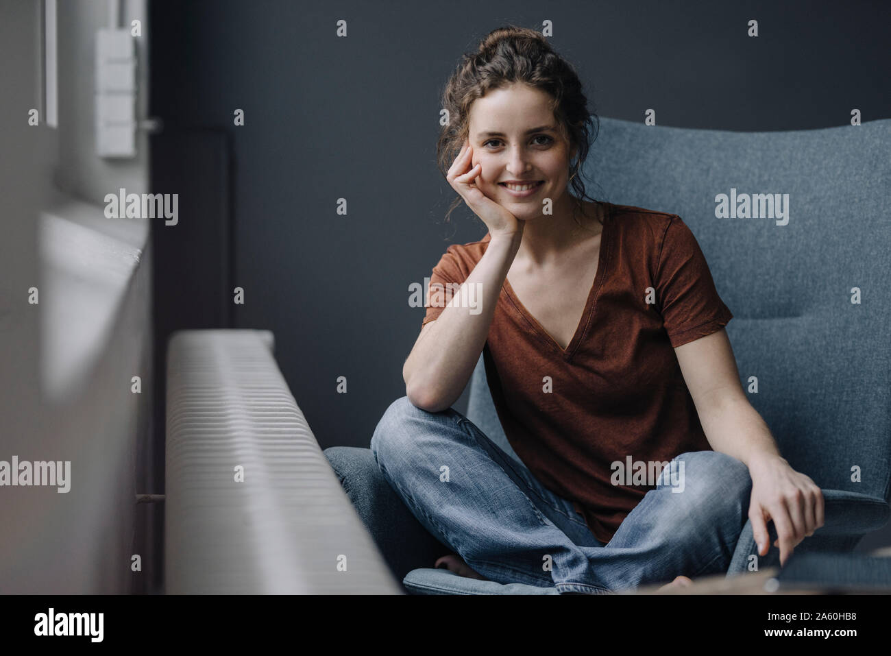 Portrait of smiling young woman sitting on lounge chair at home Stock ...