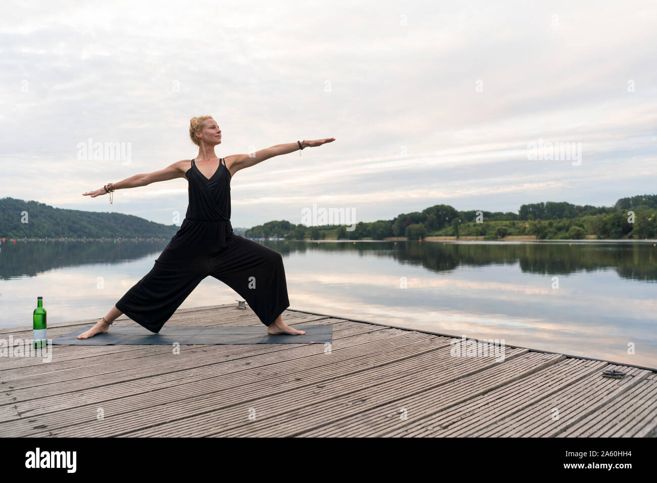 Young woman practicing yoga on a jetty at a lake Stock Photo