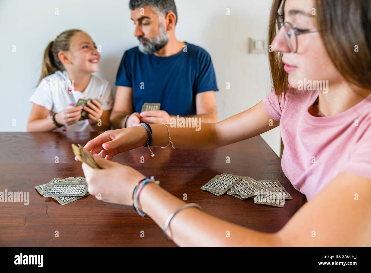 Father with two daughters playing cards on wooden table at home Stock Photo