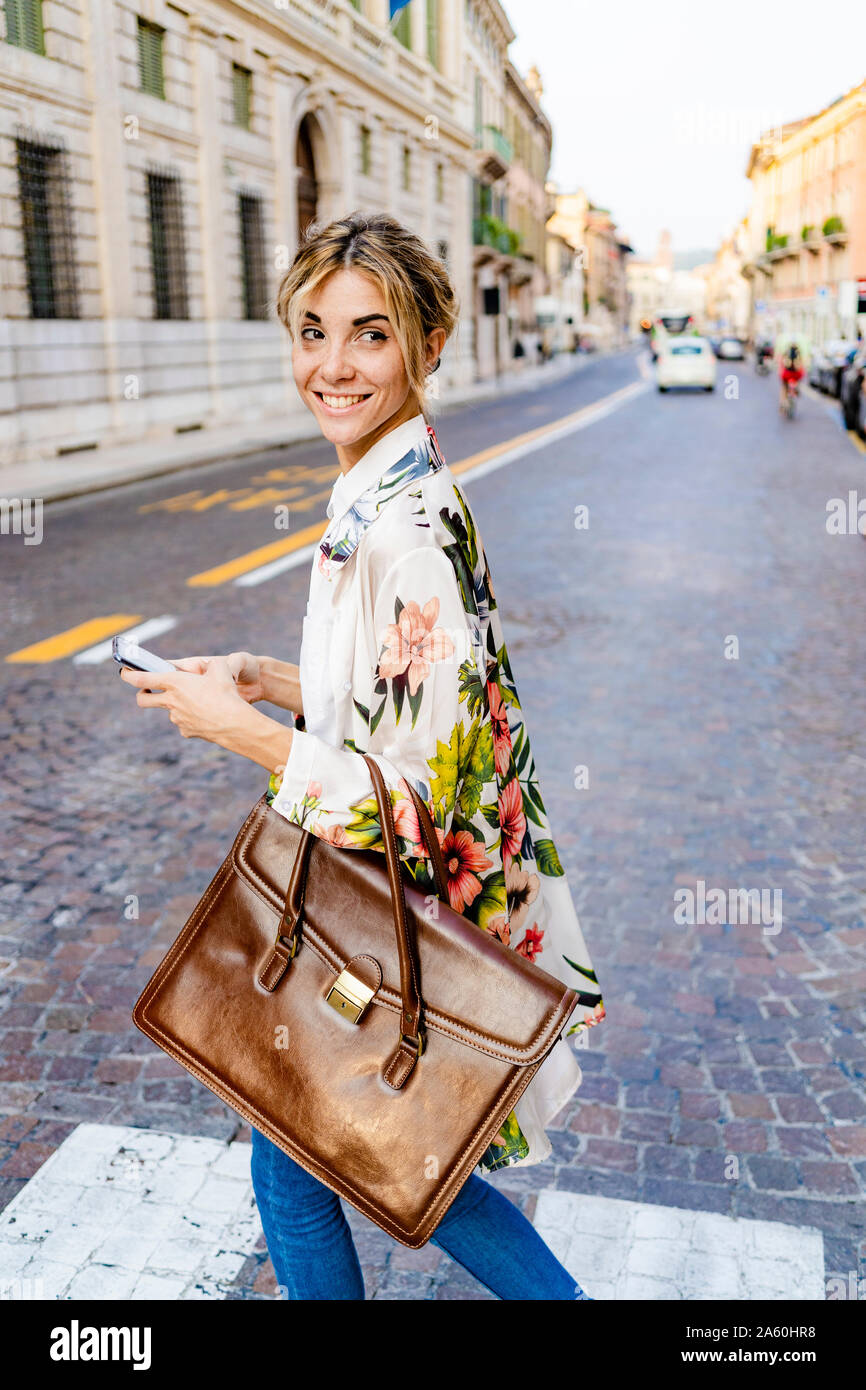 Smiling woman with smartphone walking through the city Stock Photo