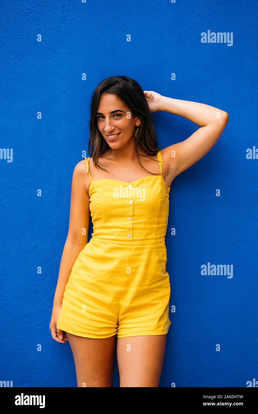 Portrait of beautiful young woman in yellow dress posing at a blue wall Stock Photo