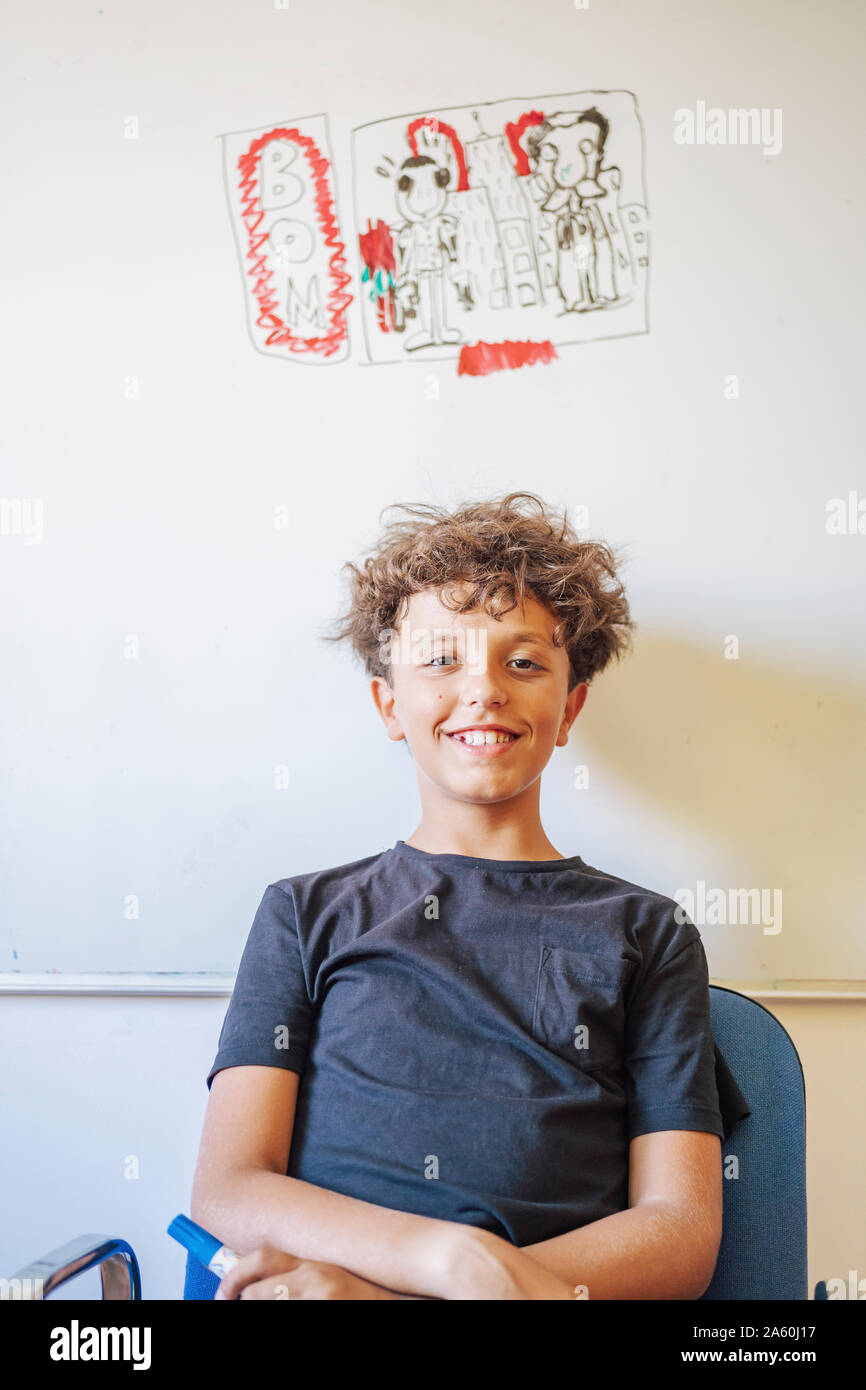 Portrait of smiling boy sitting in front of drawing on a whiteboard Stock Photo