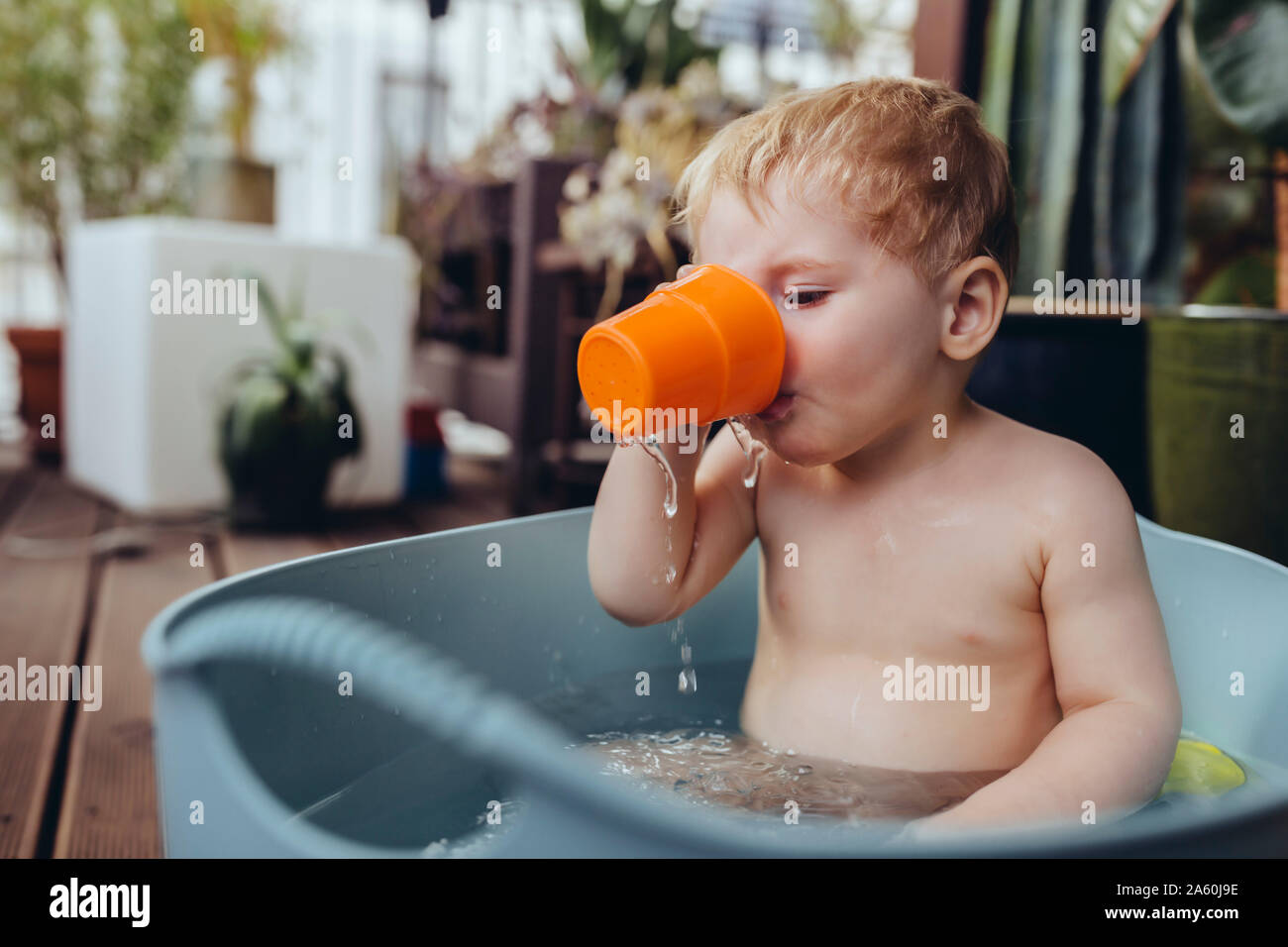 Baby boy sitting in baby bath on the balcony, drinking water Stock Photo