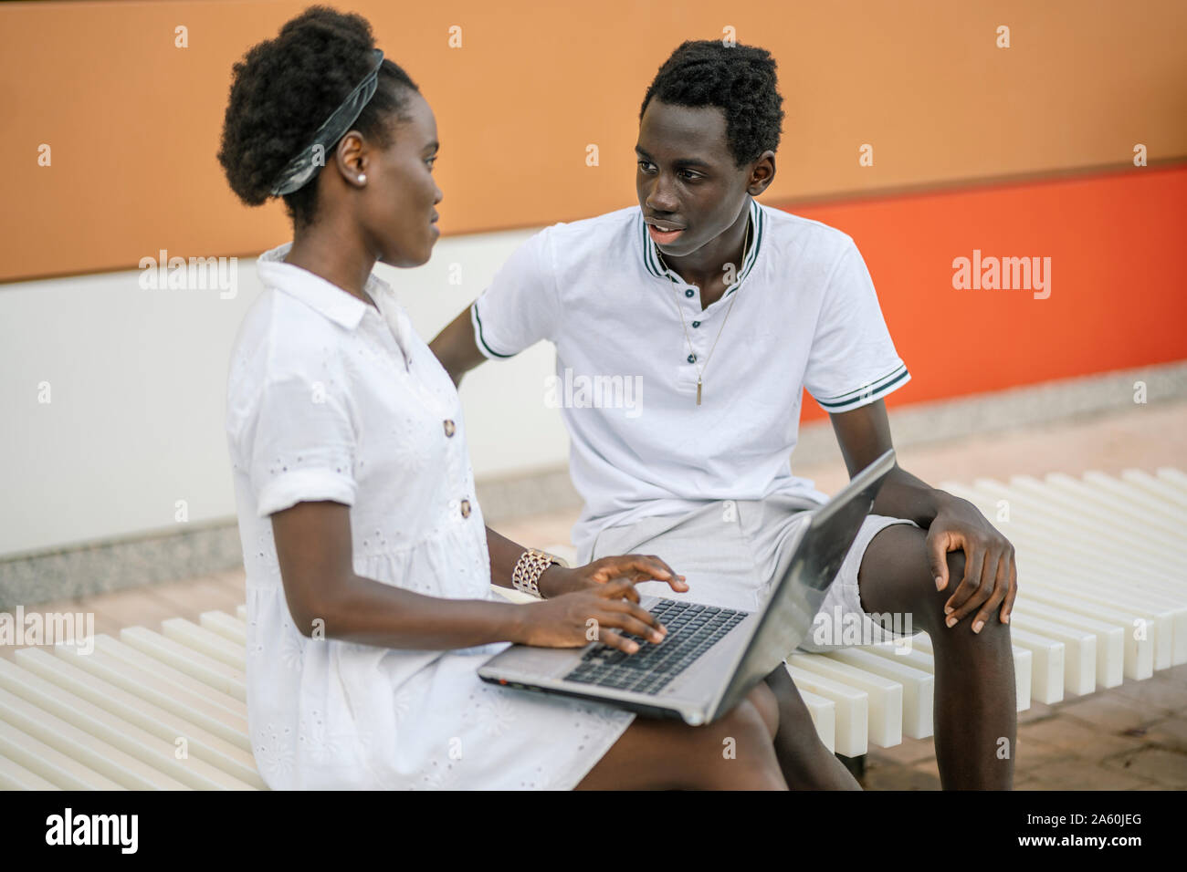 Young couple sitting on bench with laptop Stock Photo - Alamy