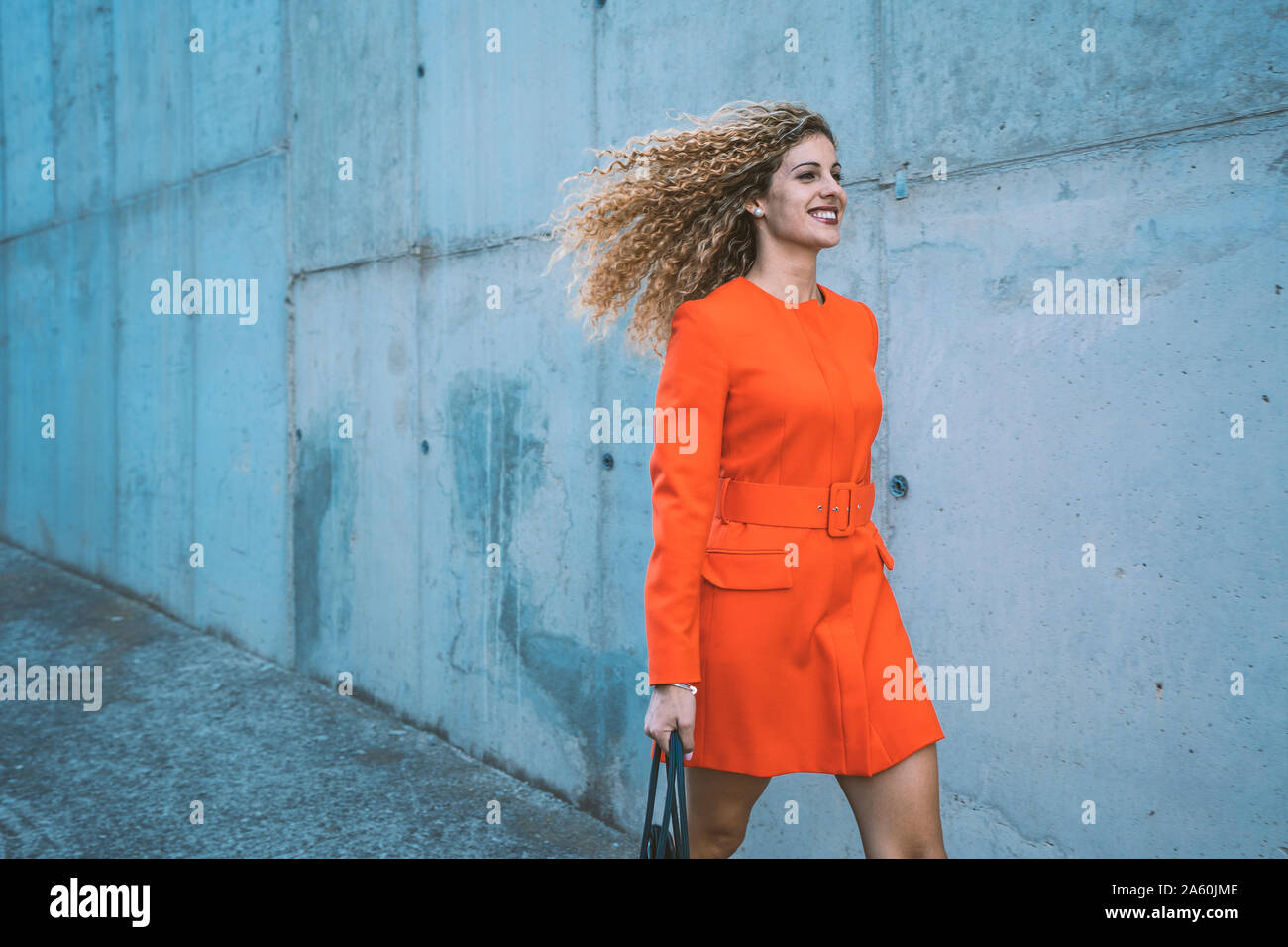 Happy young woman wearing red dress walking along street Stock Photo