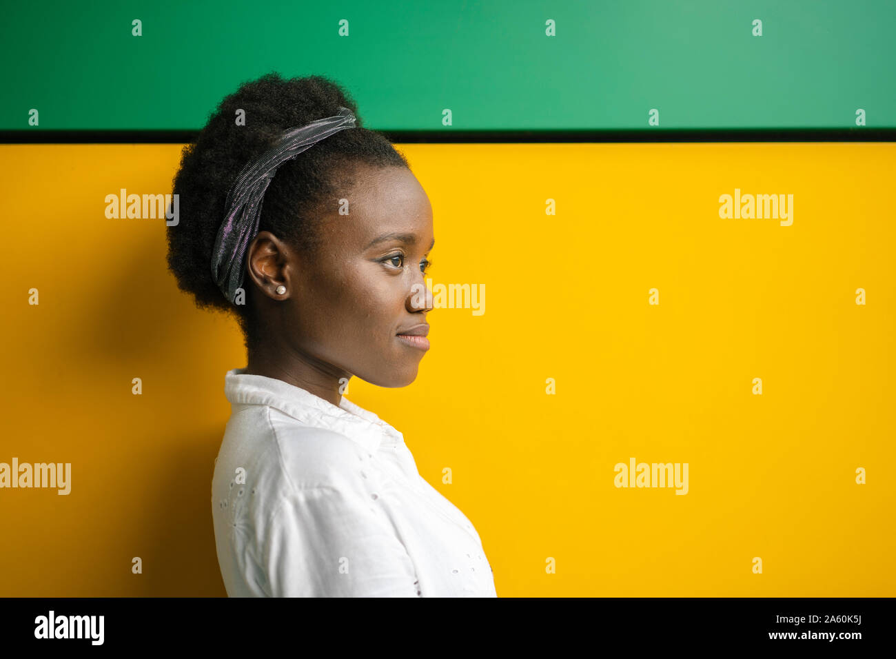 Portrait of young woman in front of yellow and green wall looking at distance Stock Photo