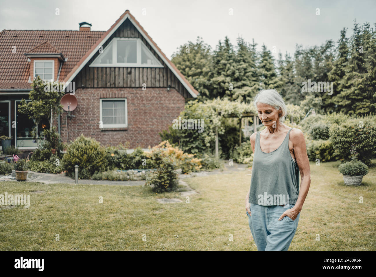 Senior woman walking her garden, with hands in pockets Stock Photo