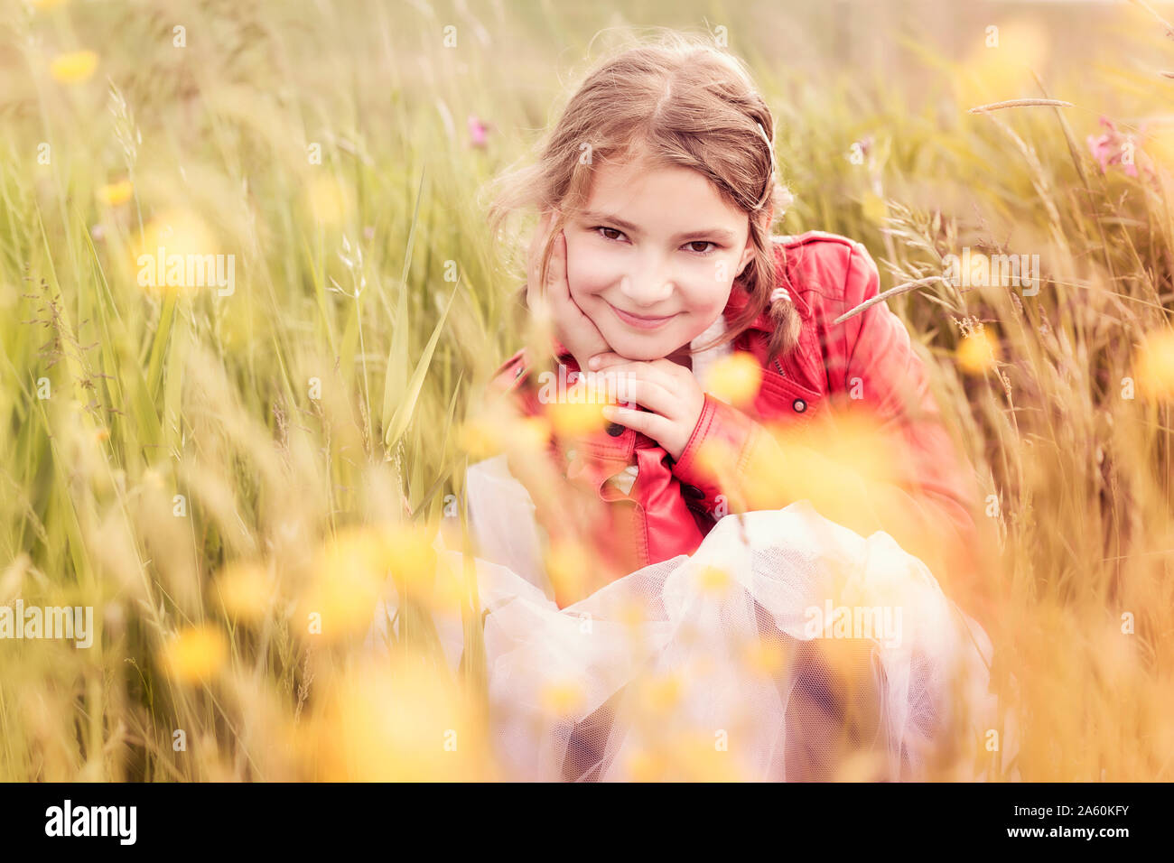 Portrait of smiling girl wearing red leather jacket crouching in flower meadow Stock Photo