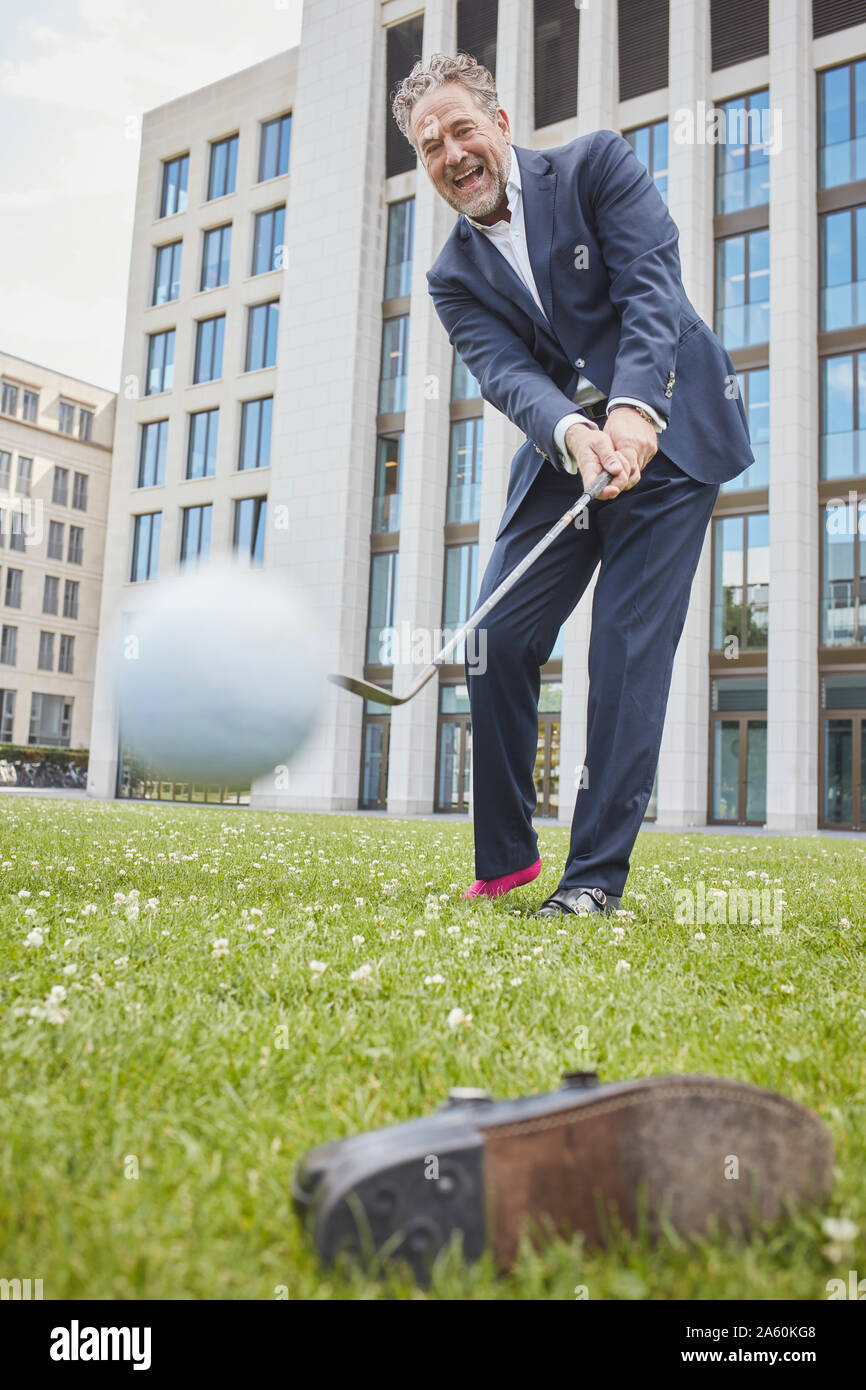 Happy mature businessman playing golf on lawn in the city Stock Photo
