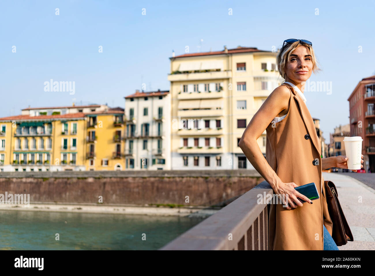 Woman with coffee to go and smartphone standing next to river in the city Stock Photo