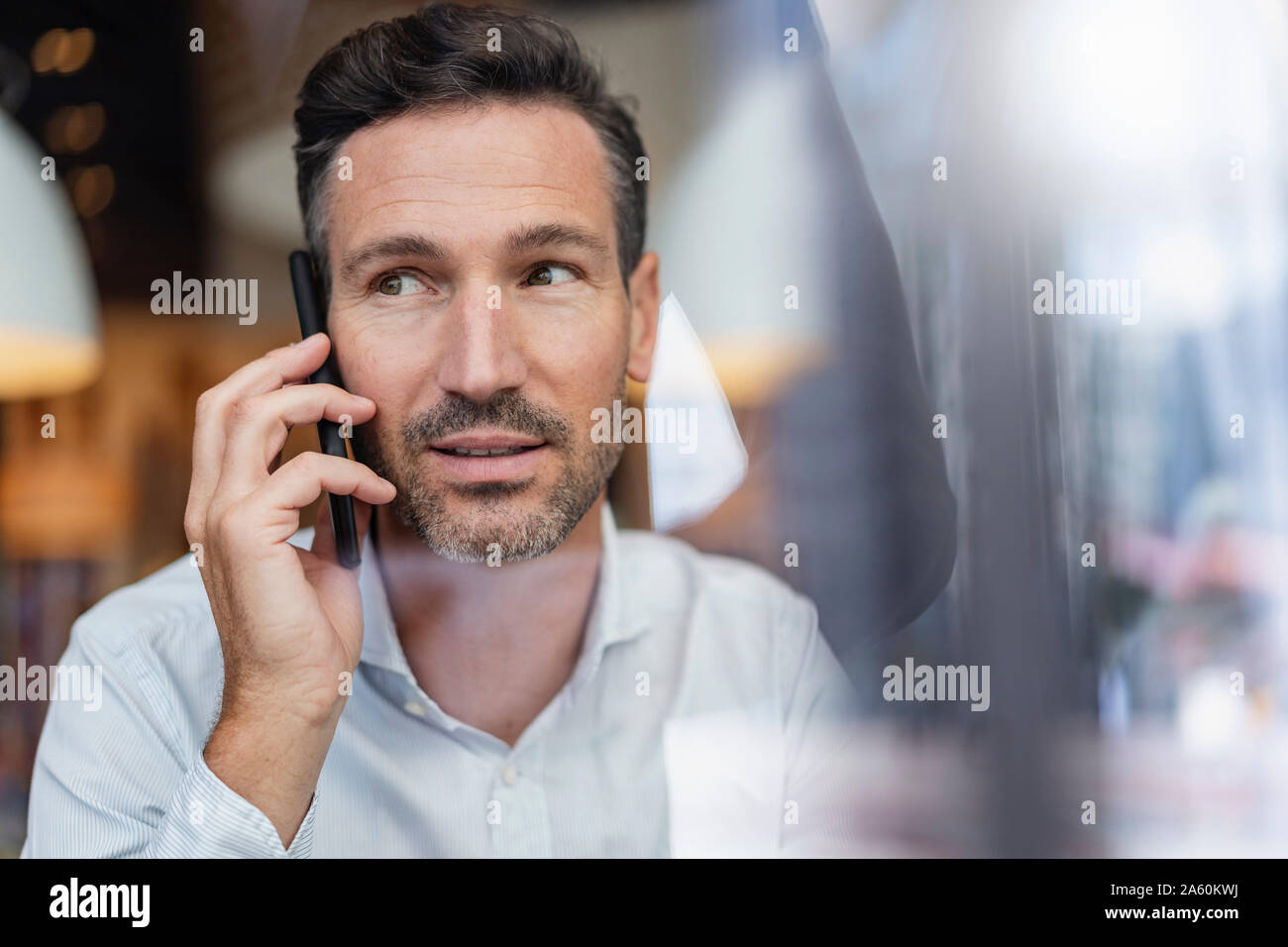 Portrait of businessman on the phone behind windowpane in a cafe Stock Photo