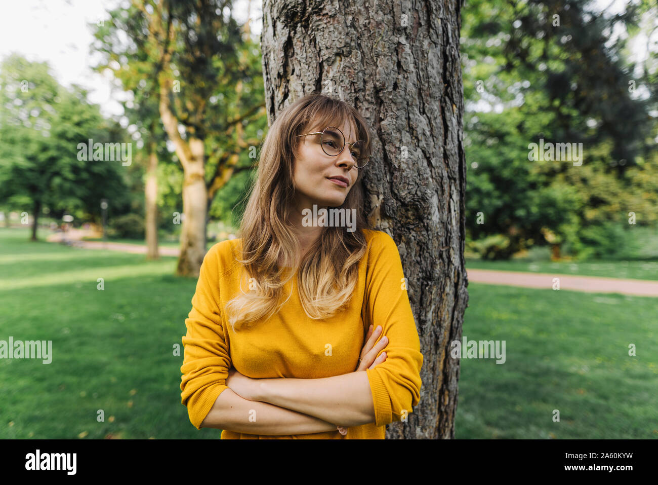 Young woman at a tree in park looking sideways Stock Photo