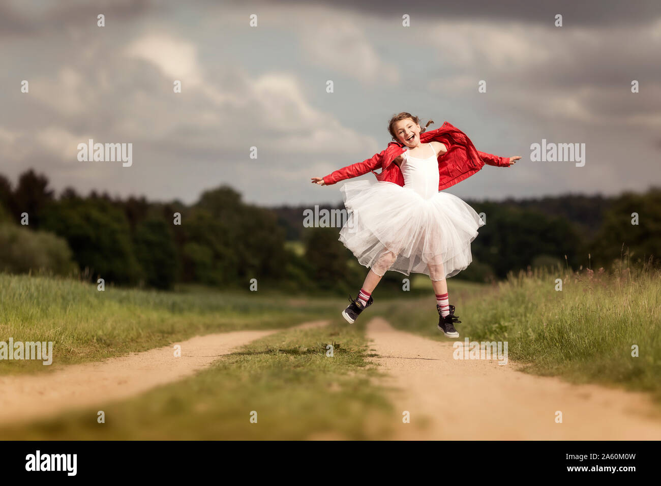 Portrait of happy girl wearing red leather jacket and tutu jumping in the air on dirt track Stock Photo