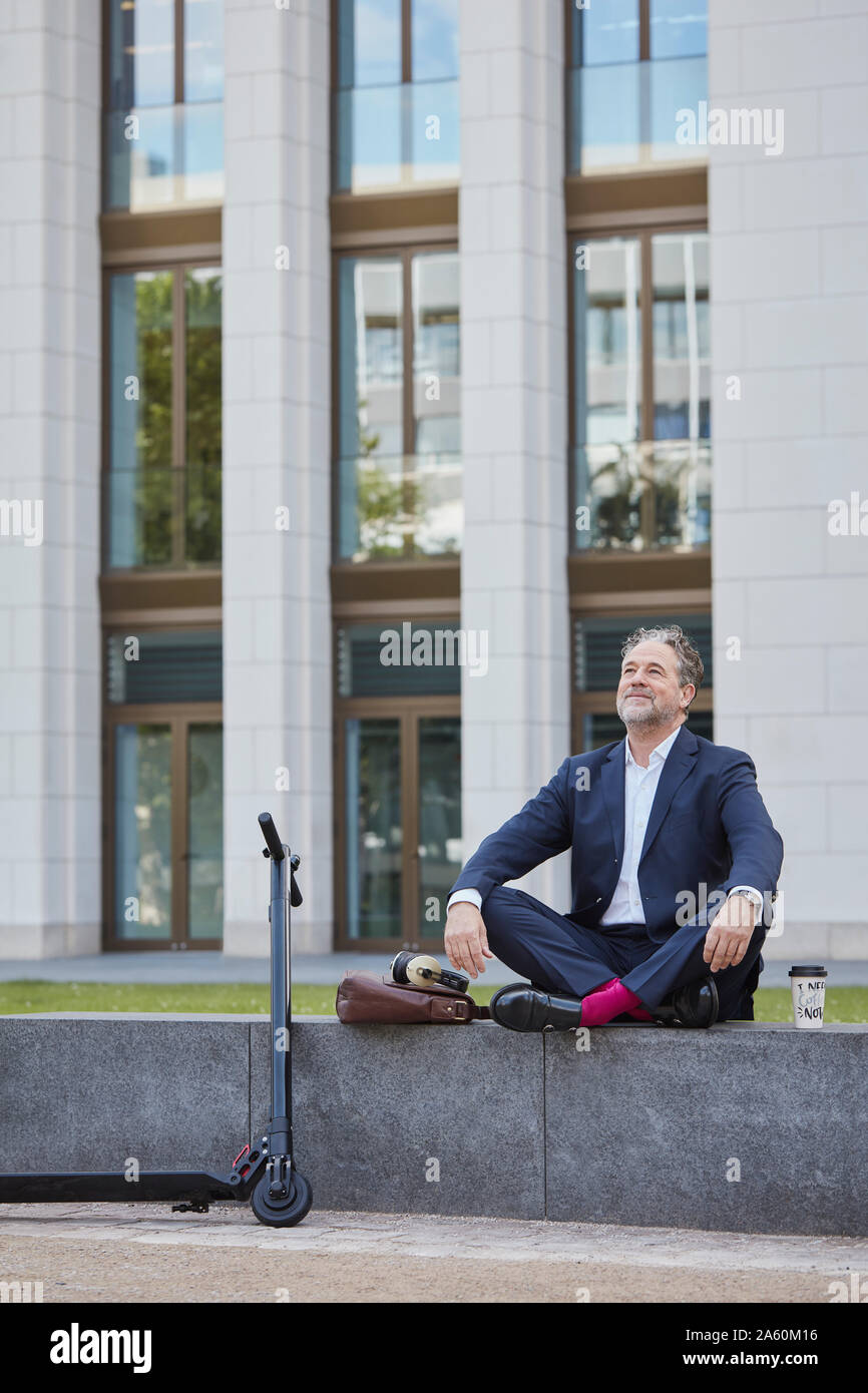 Relaxed mature businessman sitting on wall in the city Stock Photo