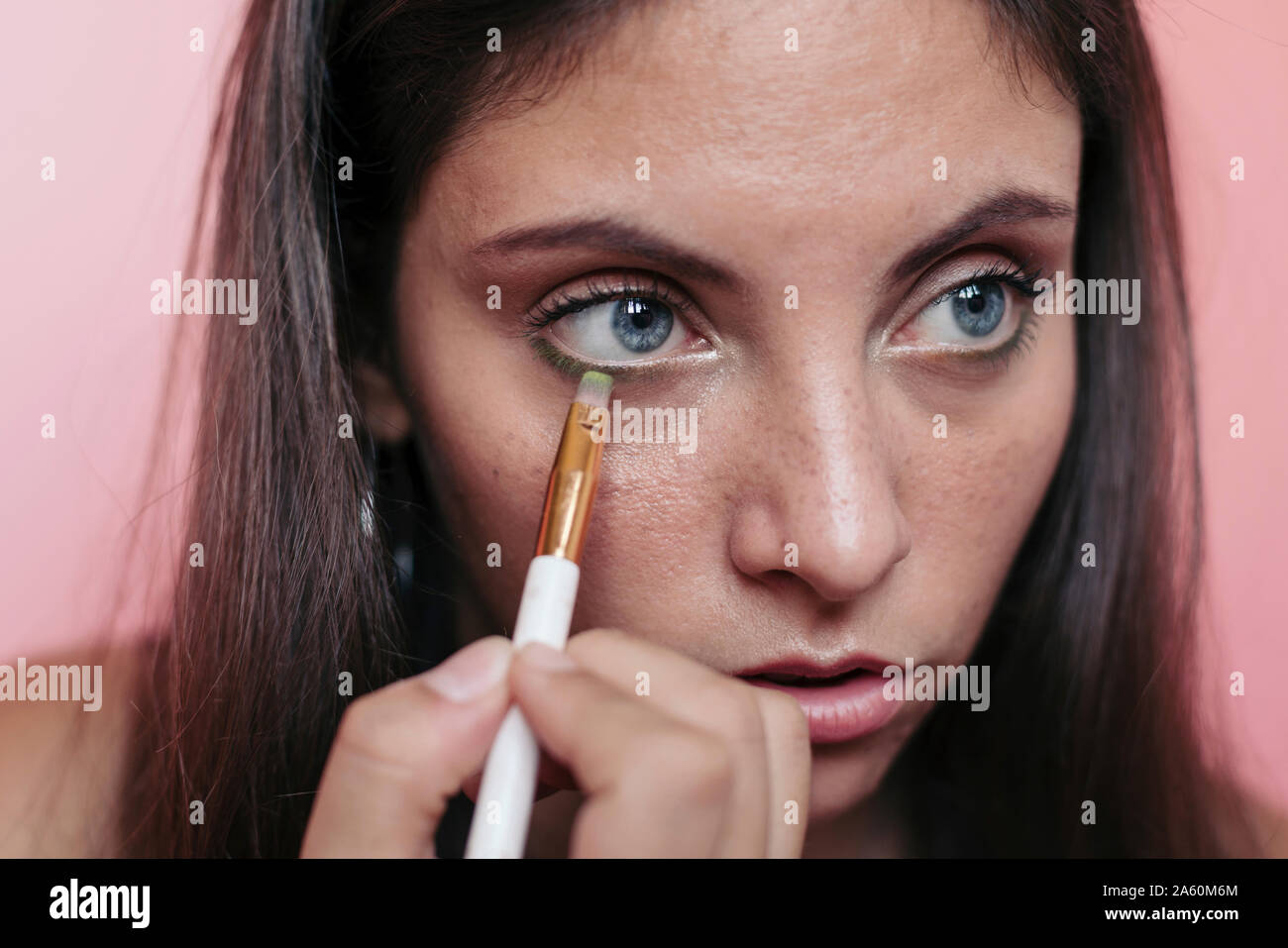 Close up of a young brunette woman with beautiful blue eyes applying eyeshadow with an eye brush Stock Photo