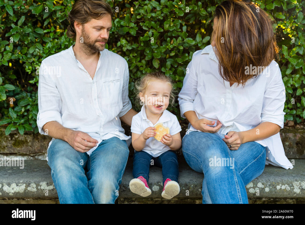 Parents with happy little daughter sitting on a bench Stock Photo