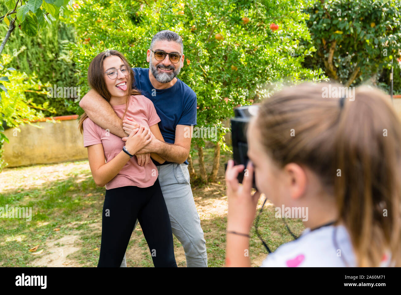 Girl taking a picture of happy father with daughter in garden Stock Photo