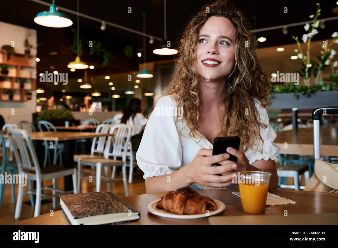 Smiling young woman with smartphone in a cafe having breakfast Stock Photo
