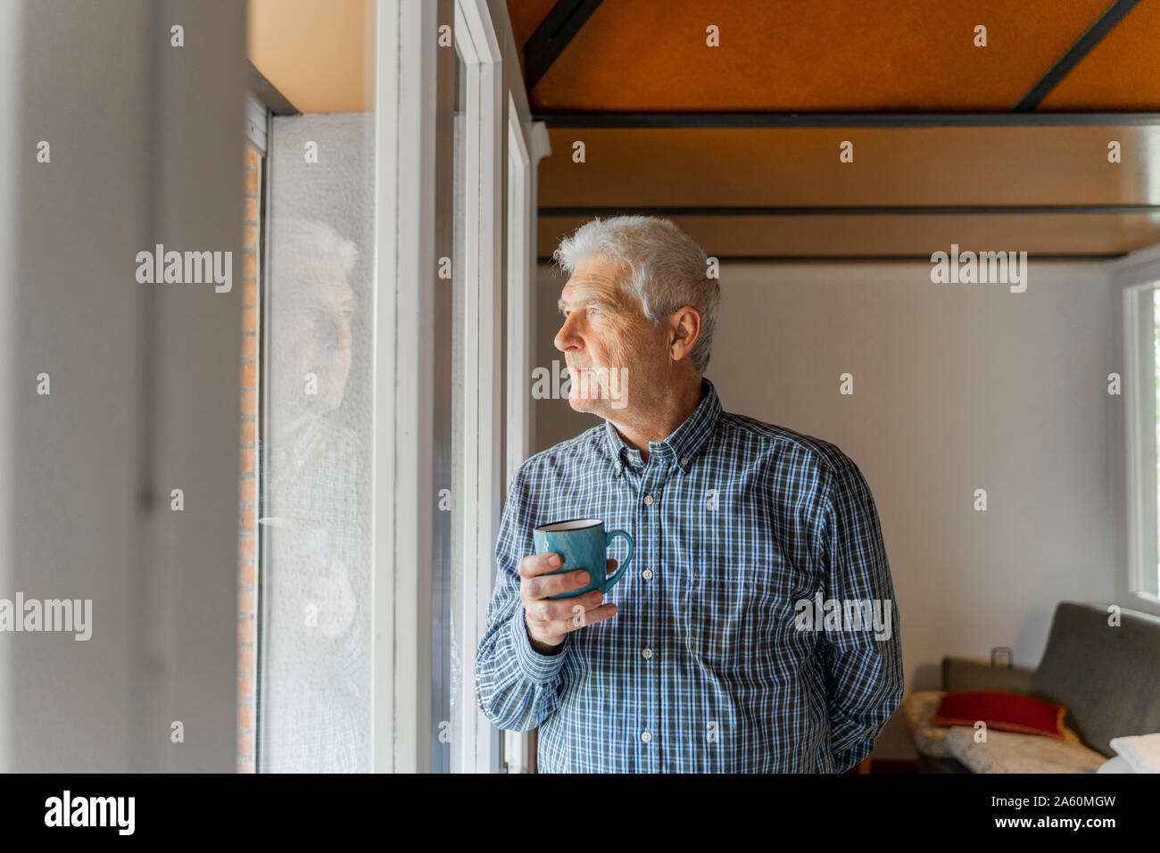 Serious senior man looking at home through window Stock Photo