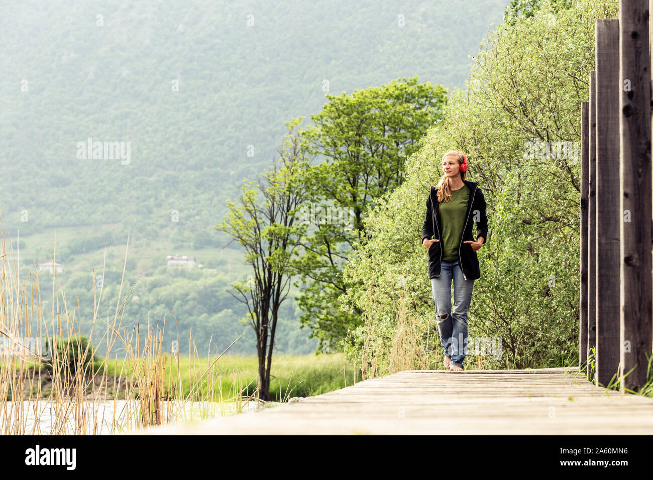 Young woman with red headphones walking on boardwalk at Lake Idro, Baitoni, Italy Stock Photo