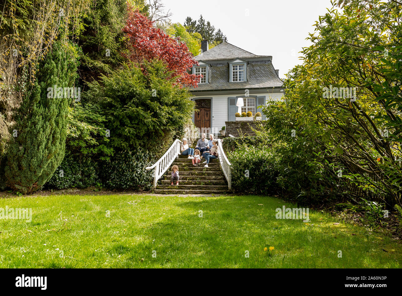 Extended family sitting on stairs in garden of their home Stock Photo