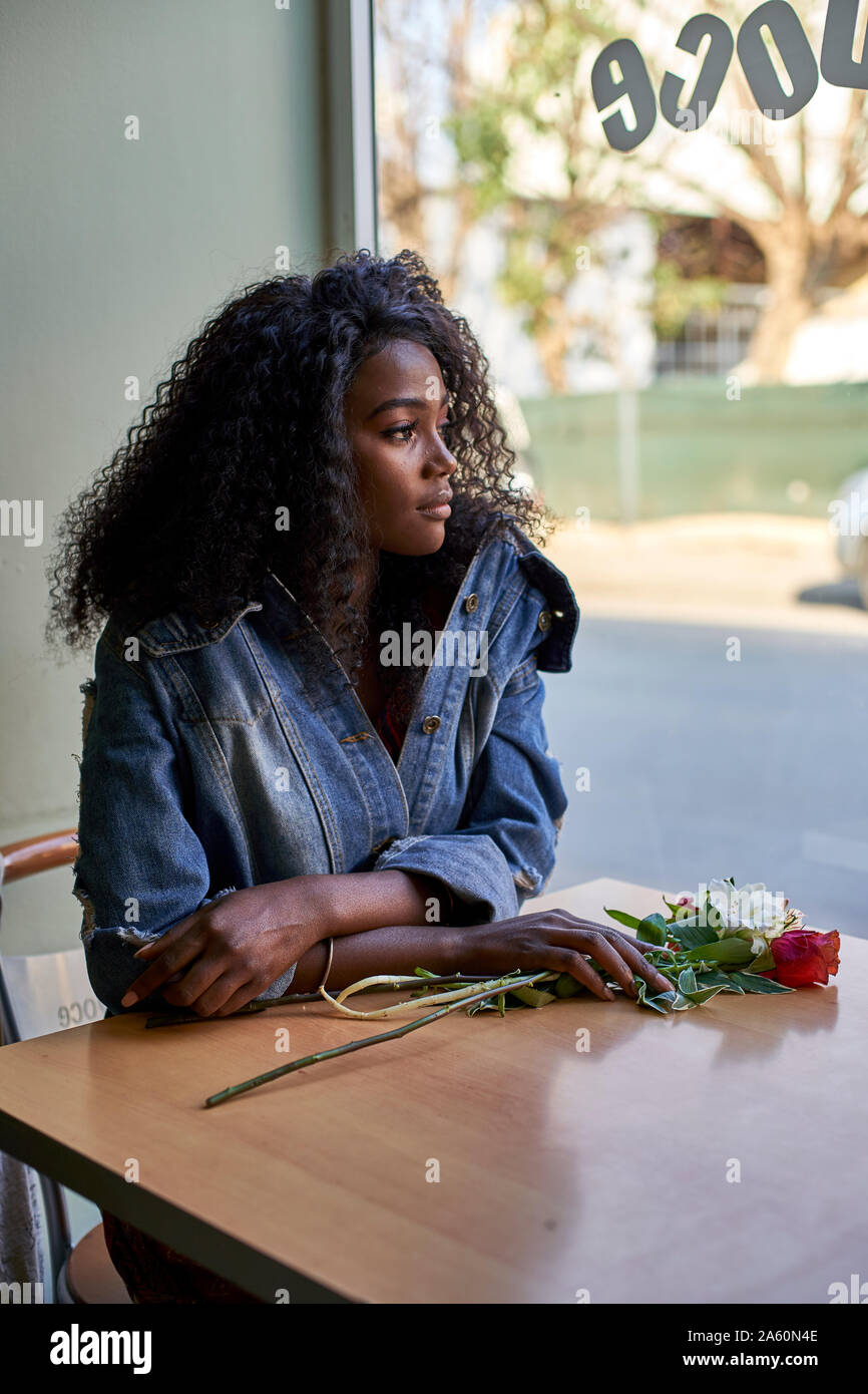 Portrait of young African woman with flowers on the table in a cafe, looking out of window Stock Photo