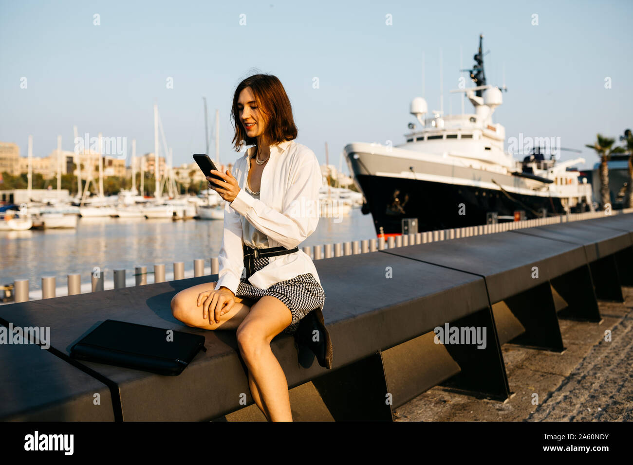 Pretty businesswoman sitting at the marina after work, using smartphone Stock Photo