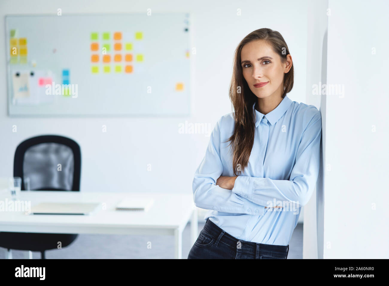Confident young businesswoman leaning against office wall looking at camera Stock Photo