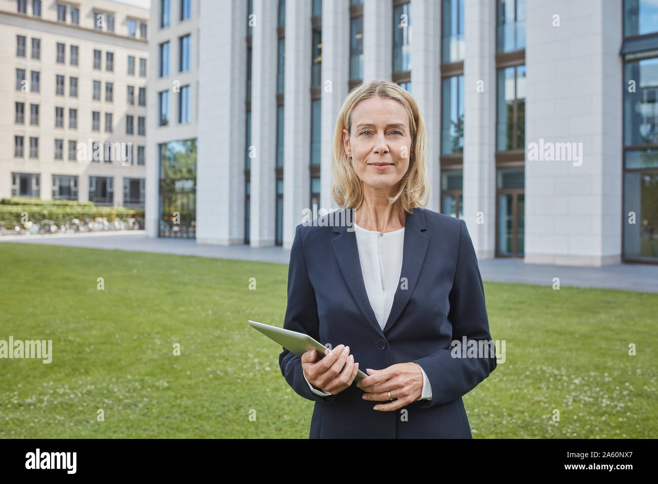 Portrait of confident businesswoman with tablet standing on lawn in the city Stock Photo
