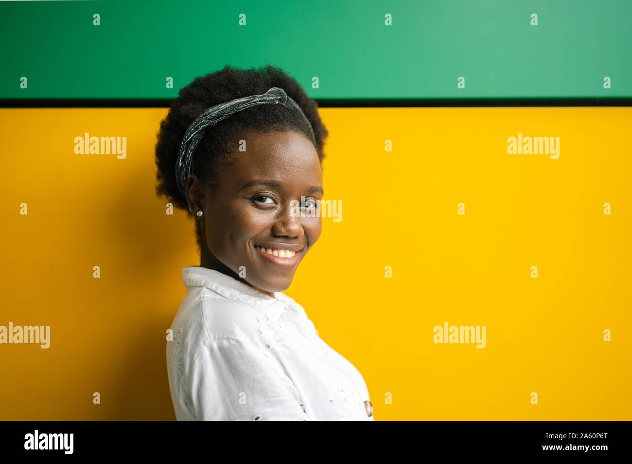 Portrait of smiling young woman in front of yellow and green wall Stock Photo