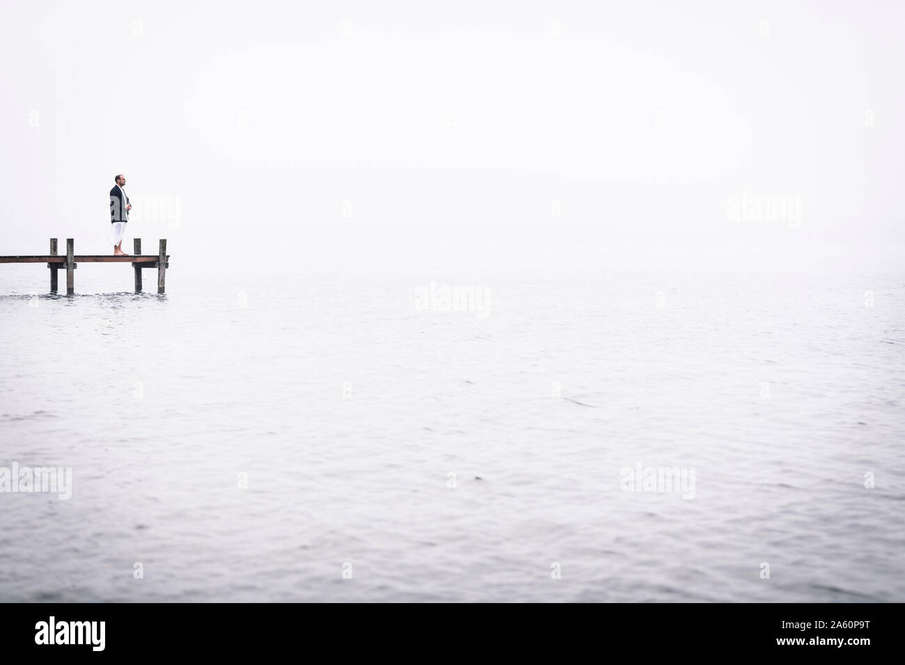 Barefoot man meditating on jetty at Lake Starnberg, Germany Stock Photo