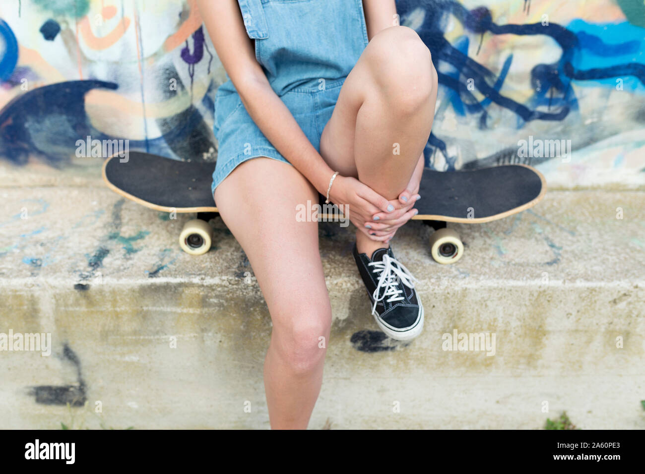 Young woman sitting on skateboard in front of graffiti Stock Photo